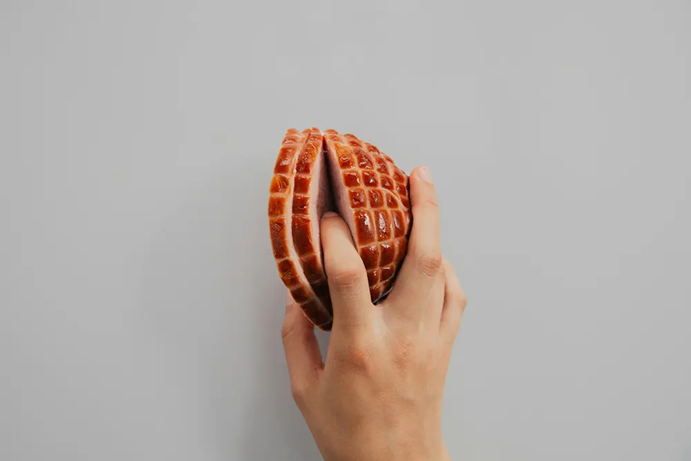 A hand holds a realistic, textured object shaped like half a waffle against a plain grey background.
